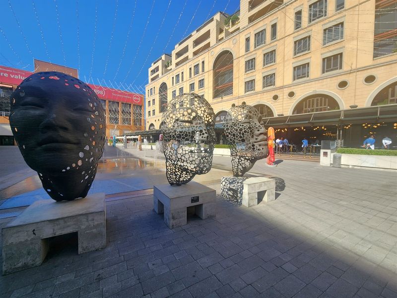 A view of a modern commercial office building exterior featuring a paved plaza and decorative sculptural installations.
