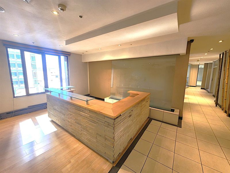 A professional office reception area featuring a built-in stone-clad desk, frosted glass partition, and a combination of tiled and laminate flooring with ample natural light.