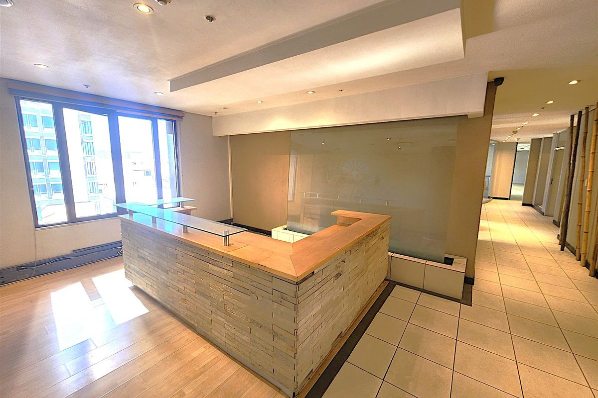 A professional office reception area featuring a built-in stone-clad desk, frosted glass partition, and a combination of tiled and laminate flooring with ample natural light.