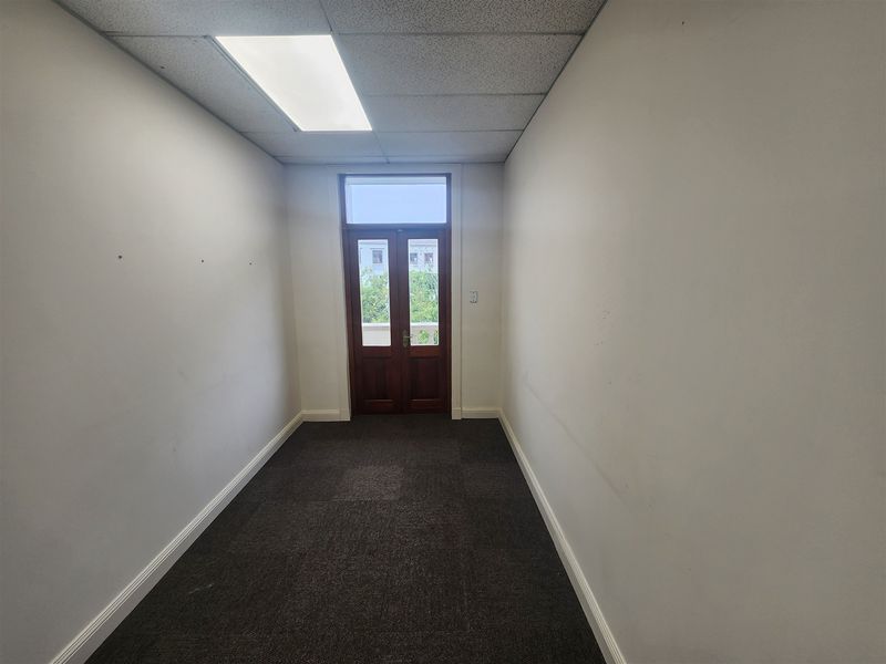 An empty office space featuring a suspended ceiling, recessed lighting, carpeted flooring, and double timber doors leading to an exterior area.