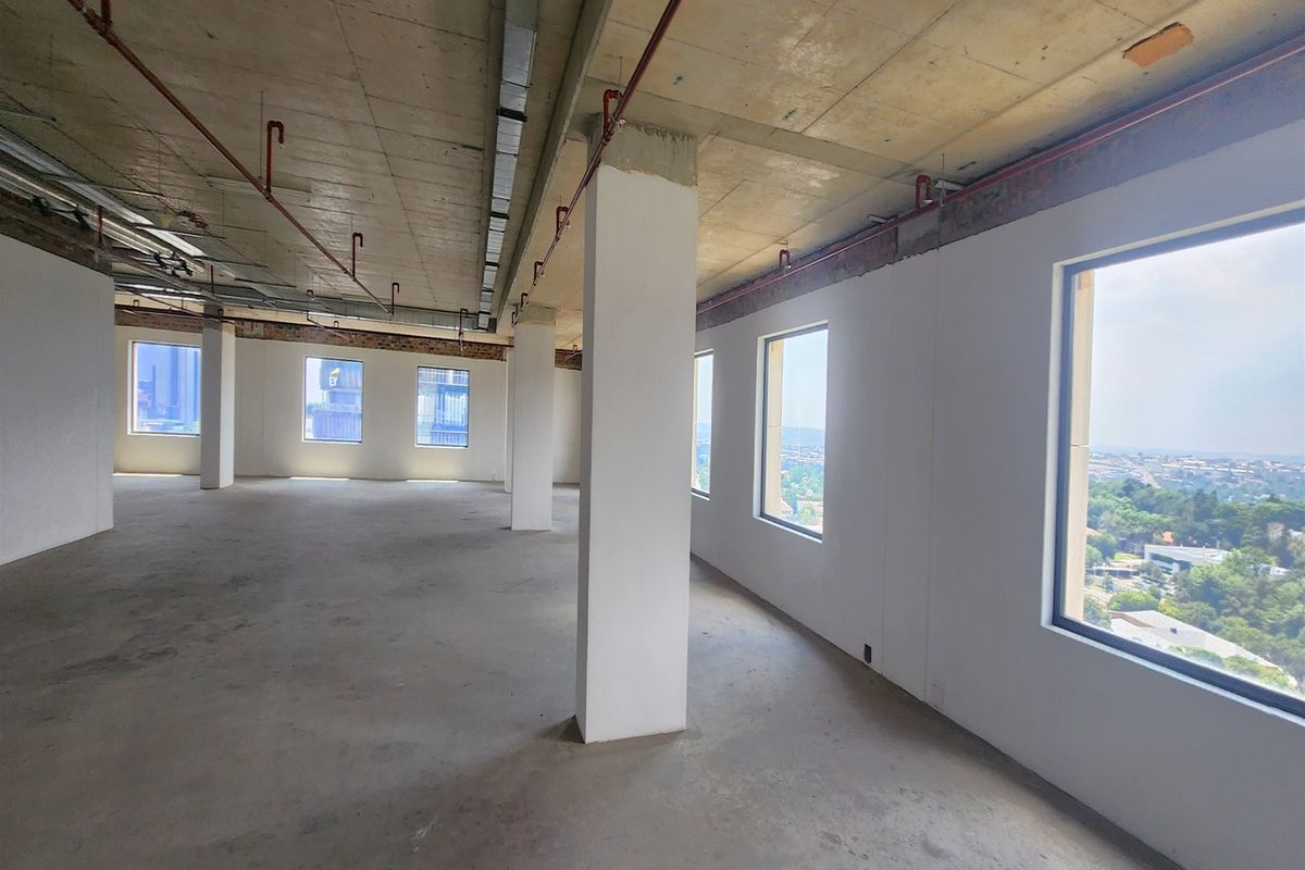 An expansive, open-plan office space featuring exposed concrete ceilings, structural columns, and large windows offering panoramic views, currently in a shell condition.