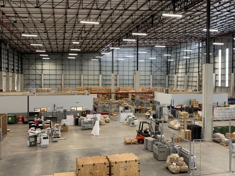 Spacious industrial warehouse featuring high ceilings with exposed steel trusses, concrete flooring, and integrated fire sprinkler systems, suitable for logistics or manufacturing operations.