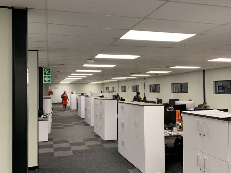 Open-plan industrial office space featuring a suspended ceiling, recessed lighting, carpet tiles, and integrated storage units.