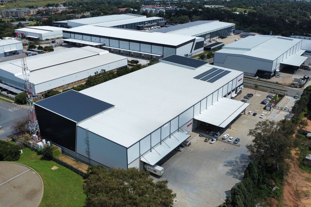 Aerial view of a large industrial warehouse complex featuring extensive metal roofing, loading bays, and paved yard space within a secure business park.
