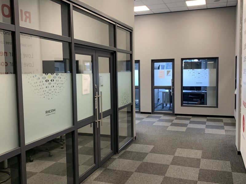 Modern industrial office hallway featuring glass partition walls, aluminium framing, carpet tile flooring, and a clean, professional aesthetic with recessed ceiling lighting.