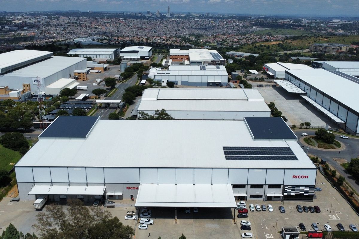 Aerial view of a large industrial warehouse facility featuring solar panels, extensive loading bays, and a paved parking area within a commercial business park.