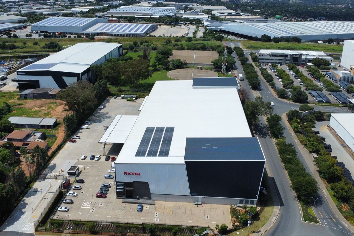 Aerial view of a modern industrial warehouse facility featuring a large roof with solar panels, dedicated parking, and secure perimeter access.