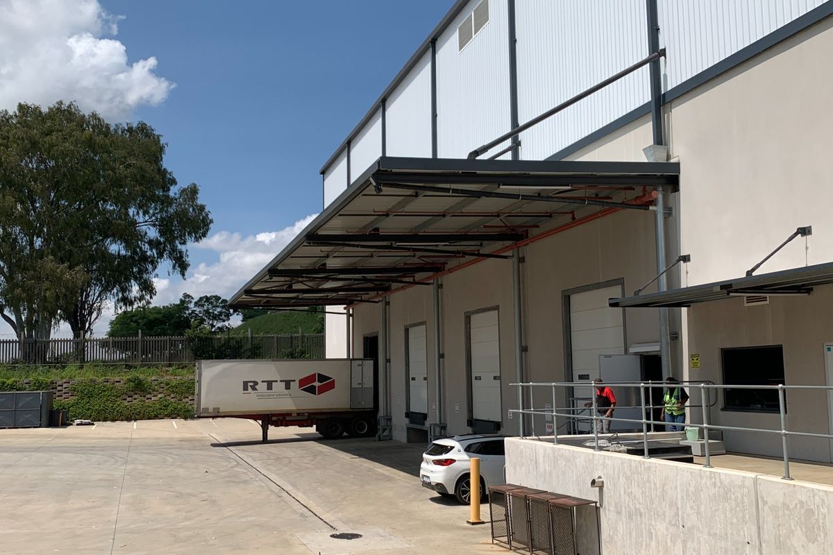 Industrial warehouse exterior featuring multiple loading docks with roller shutter doors, a large metal canopy, and a concrete loading apron.