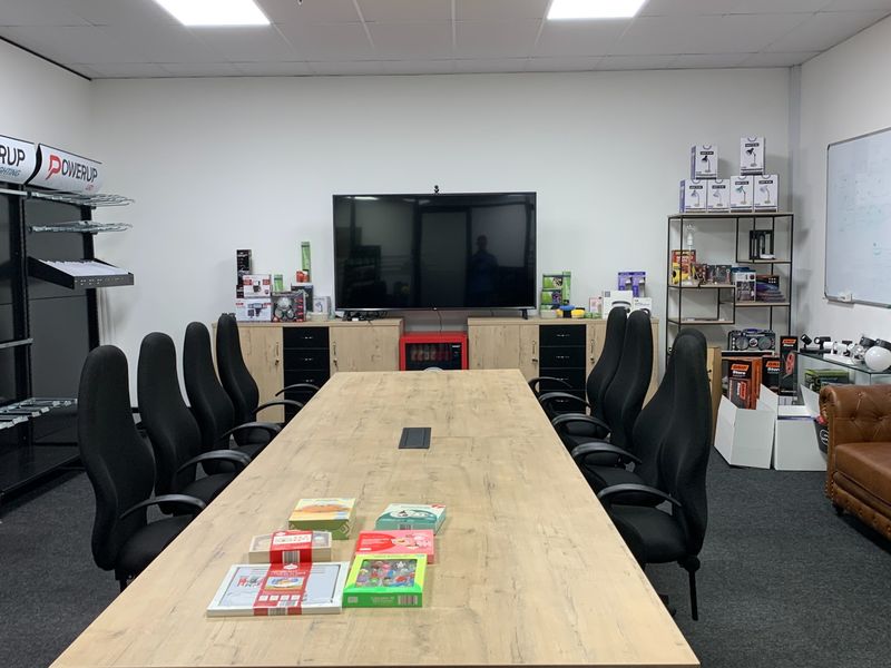 A functional office boardroom featuring a large central table, built-in storage cabinetry, recessed ceiling lighting, and a wall-mounted display screen.
