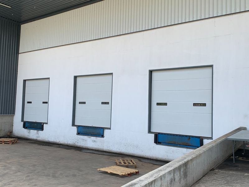 Industrial loading bay area featuring three sectional overhead doors with integrated dock levelers and a concrete loading apron.