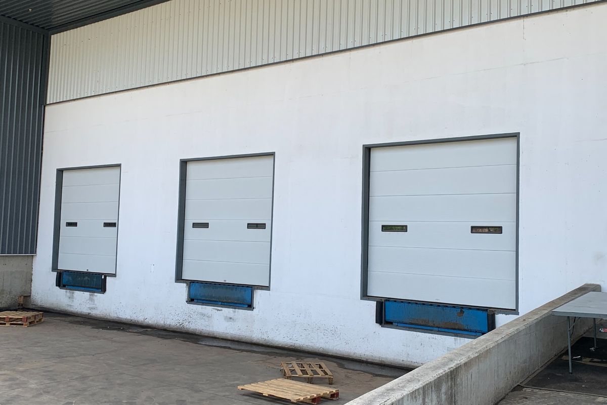 Industrial loading bay area featuring three sectional overhead doors with integrated dock levelers and a concrete loading apron.