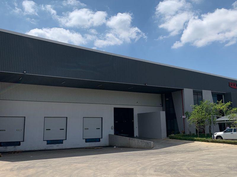 Industrial warehouse exterior featuring multiple loading docks with roller shutter doors, concrete loading apron, and modern metal cladding facade.