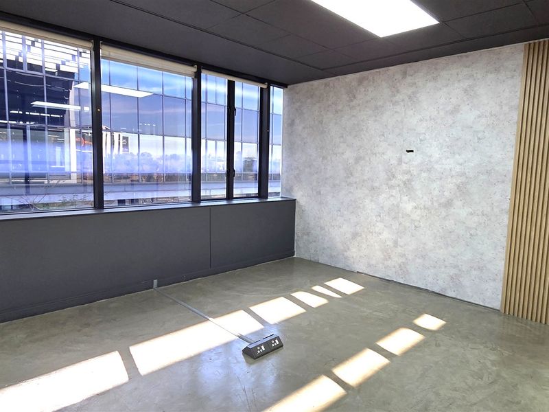 Modern empty office space featuring polished concrete floors, timber slat wall accents, and large windows providing ample natural light.