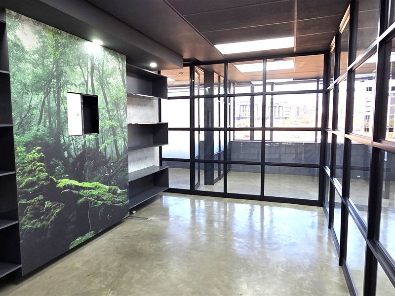 Modern office space featuring polished concrete floors, extensive glass partitioning, and built-in shelving with a decorative forest-themed feature wall.