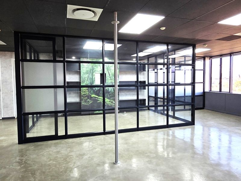 Modern open-plan office space featuring polished concrete floors, contemporary black-framed glass partitions, and integrated shelving, offering a professional and bright work environment.