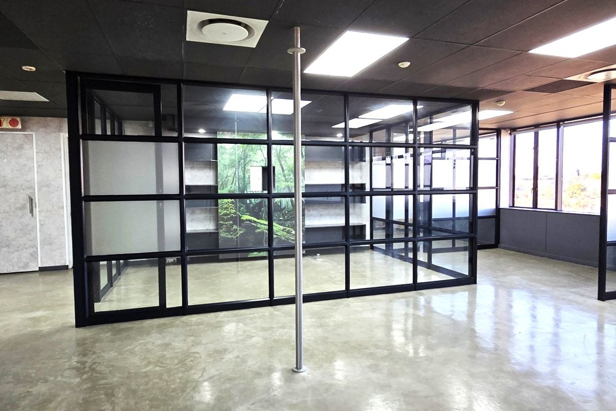 Modern open-plan office space featuring polished concrete floors, contemporary black-framed glass partitions, and integrated shelving, offering a professional and bright work environment.