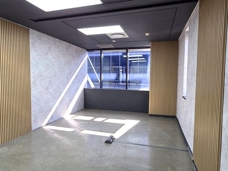 A modern, empty office space featuring polished concrete floors, contemporary timber slat wall accents, and a large glass partition wall.