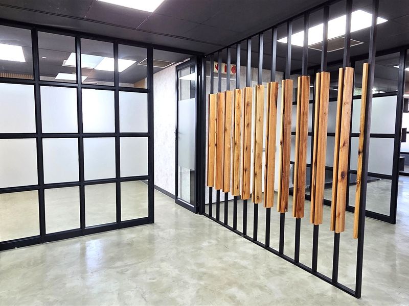 Modern office space featuring polished concrete floors, black metal-framed glass partitions, and a decorative timber slat feature wall.