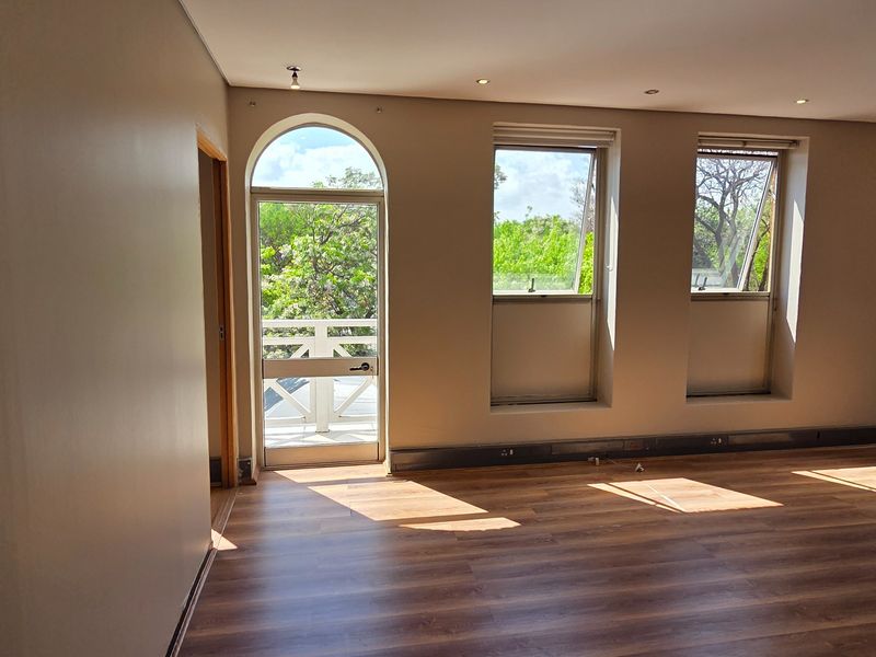 A bright, empty office space featuring laminate flooring, recessed lighting, and an arched glass door leading to an outdoor balcony area.