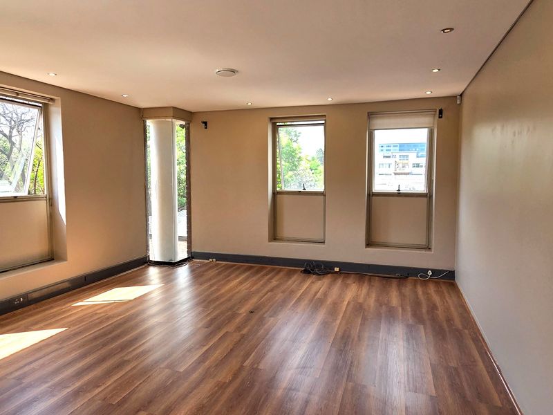 A bright, vacant office space featuring modern laminate flooring, recessed downlighting, and multiple windows providing natural light and exterior views.