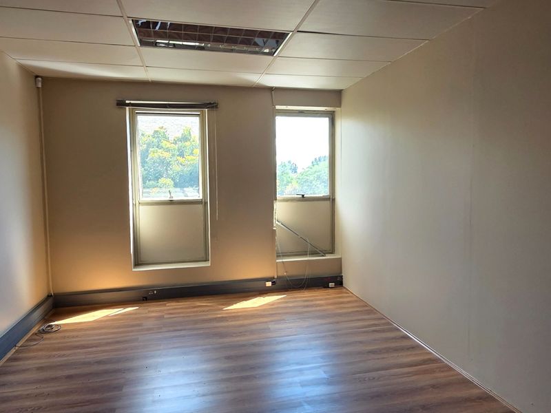 An empty office space featuring laminate flooring, suspended ceiling with recessed lighting, and dual windows providing natural light.