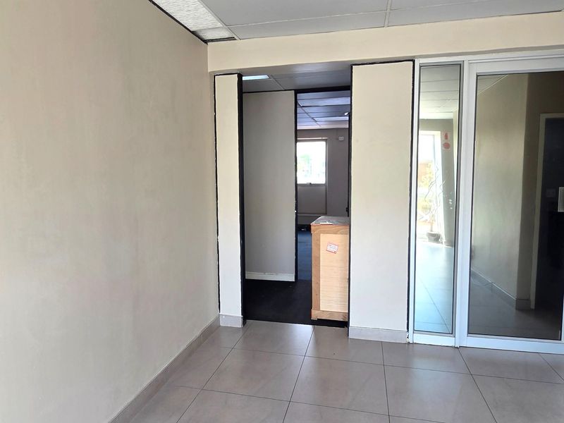 An empty office space featuring tiled flooring, a suspended ceiling, and glass partition doors, offering a clean and functional layout for professional use.