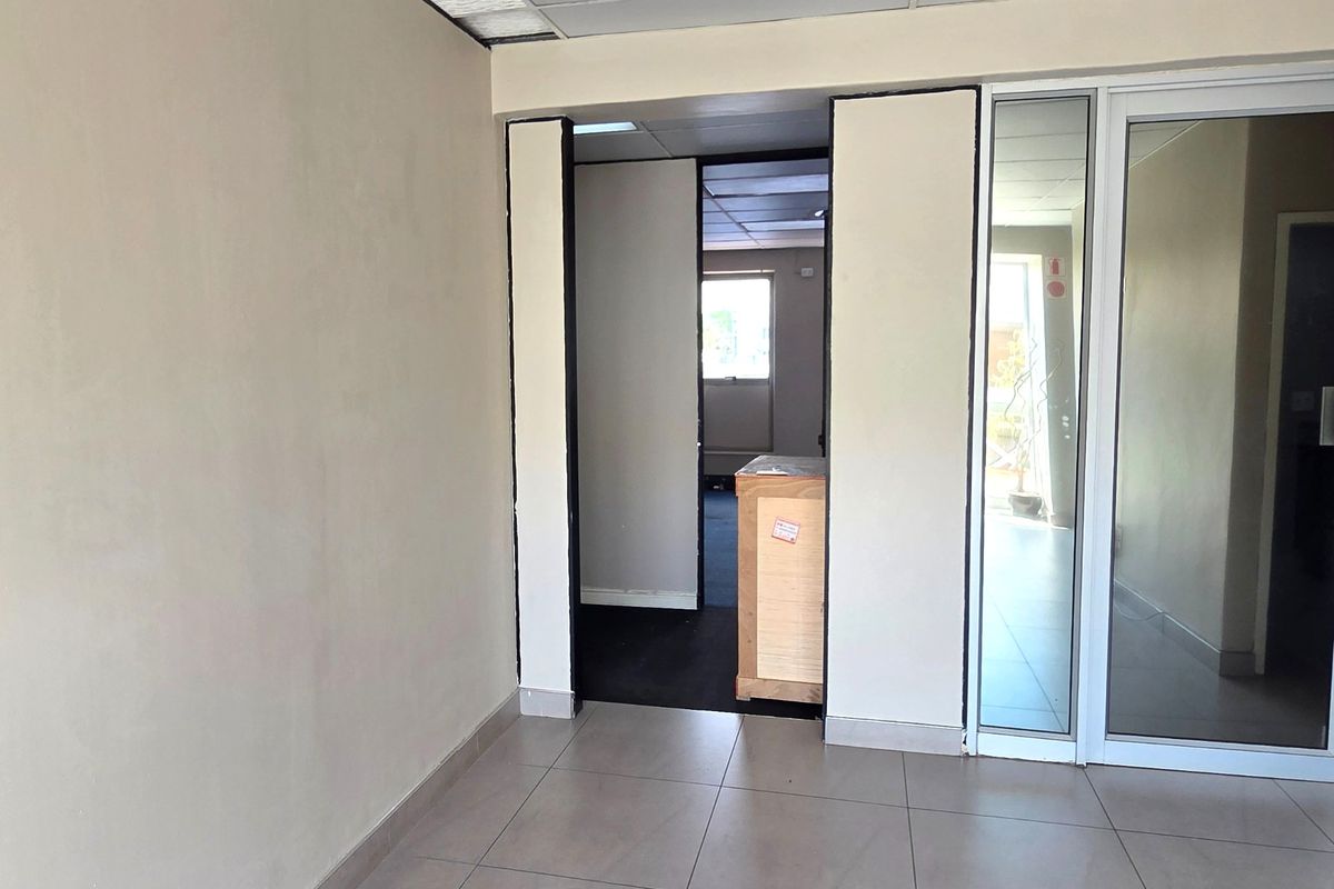An empty office space featuring tiled flooring, a suspended ceiling, and glass partition doors, offering a clean and functional layout for professional use.