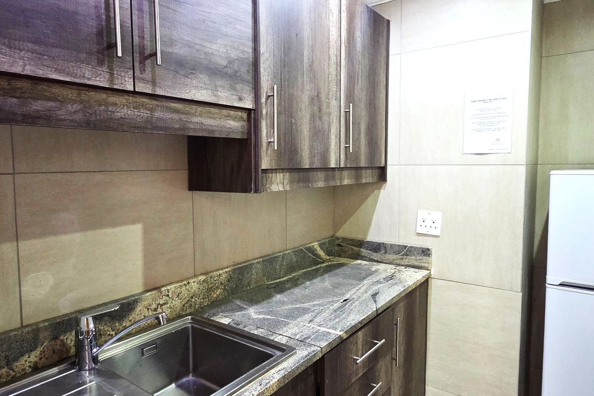 A compact office kitchenette featuring modern wood-grain cabinetry, granite countertops, and a stainless steel sink with a mixer tap.