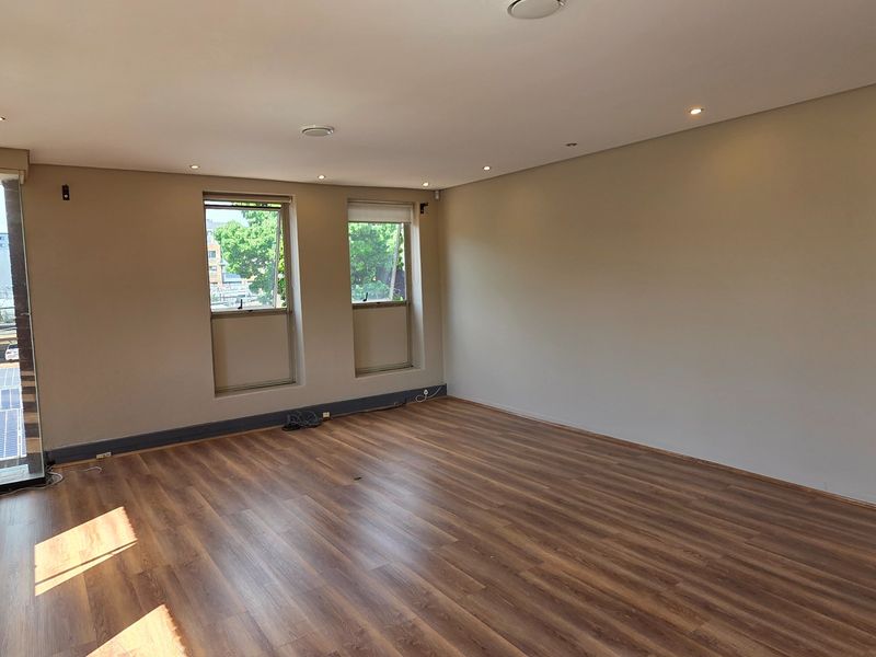 A bright, empty office space featuring modern laminate flooring, recessed downlighting, and large windows providing natural light.