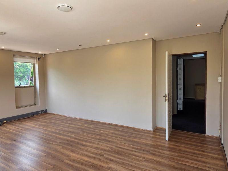 A bright, empty office space featuring modern laminate flooring, recessed downlighting, and neutral wall finishes, providing a clean and versatile professional work environment.