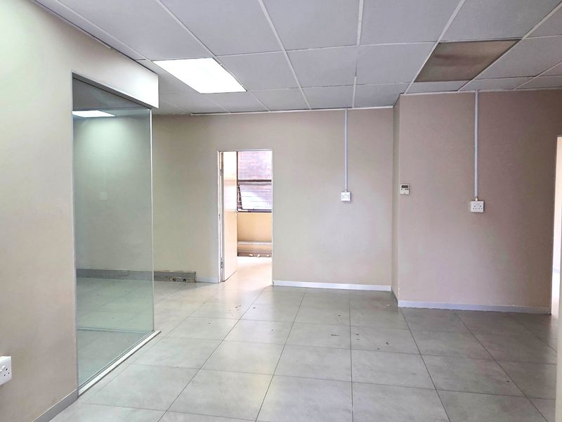 An empty office space featuring tiled flooring, a suspended ceiling with recessed lighting, and a glass partition wall.