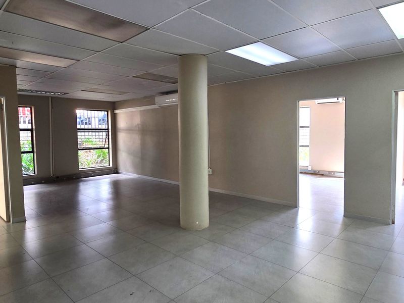 Spacious, open-plan office area featuring ceramic tile flooring, a central structural column, suspended ceiling with recessed lighting, and integrated air conditioning.