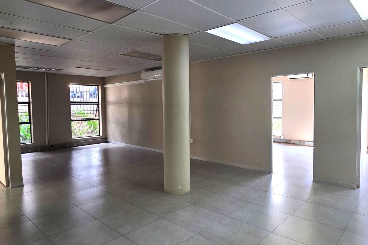 Spacious, open-plan office area featuring ceramic tile flooring, a central structural column, suspended ceiling with recessed lighting, and integrated air conditioning.