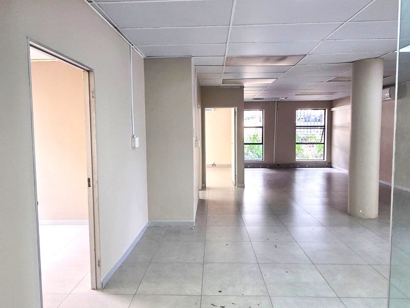 Open plan office space featuring tiled flooring, a suspended ceiling, and large windows with security bars, offering a functional and versatile workspace.