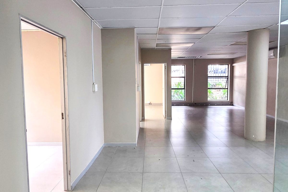 Open plan office space featuring tiled flooring, a suspended ceiling, and large windows with security bars, offering a functional and versatile workspace.