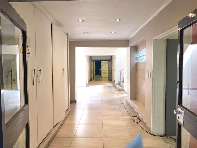 A bright, spacious office hallway featuring tiled flooring, recessed downlighting, and extensive built-in storage cupboards.
