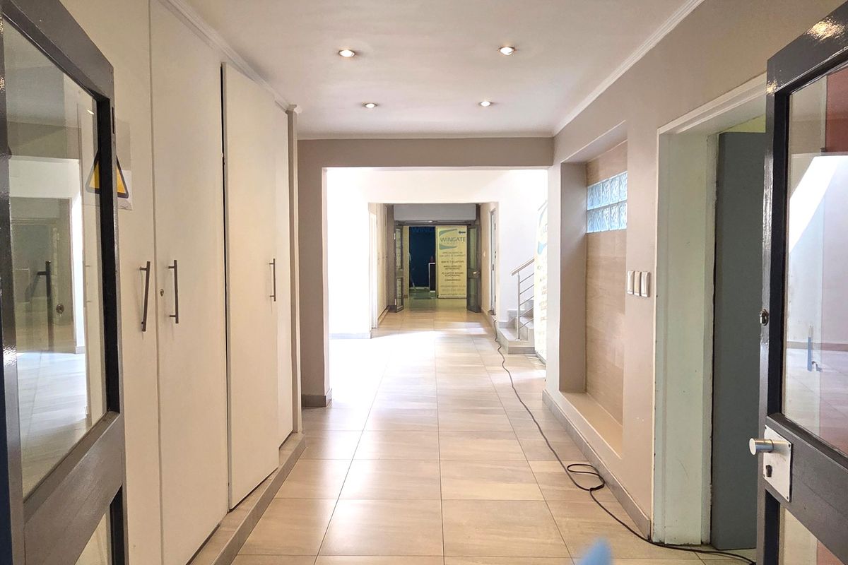 A bright, spacious office hallway featuring tiled flooring, recessed downlighting, and extensive built-in storage cupboards.