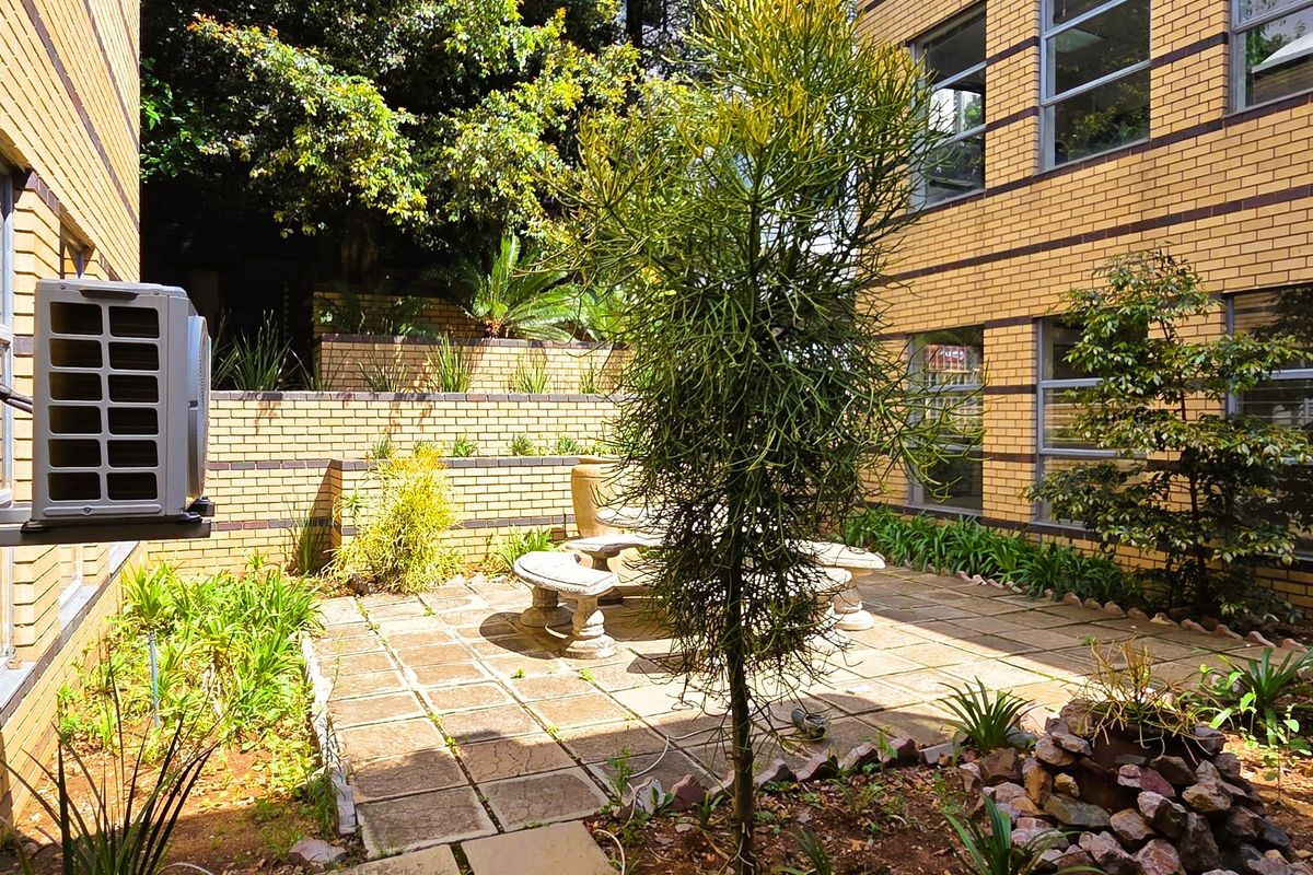 A well-maintained rear courtyard featuring paved patio space, brick retaining walls, and established landscaping, adjacent to the office building facade.