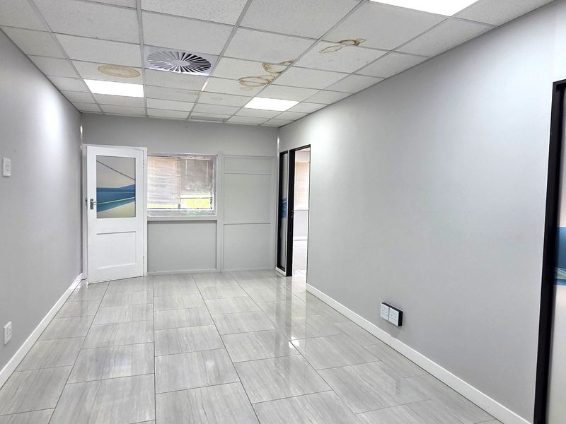 An empty office space featuring tiled flooring, a suspended ceiling with recessed lighting, and visible water damage on the ceiling tiles.