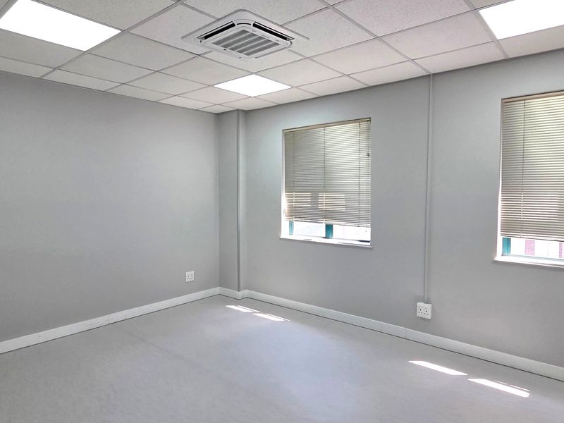 A clean, empty office space featuring a suspended ceiling, recessed lighting, integrated cassette air conditioning, and windows fitted with venetian blinds.