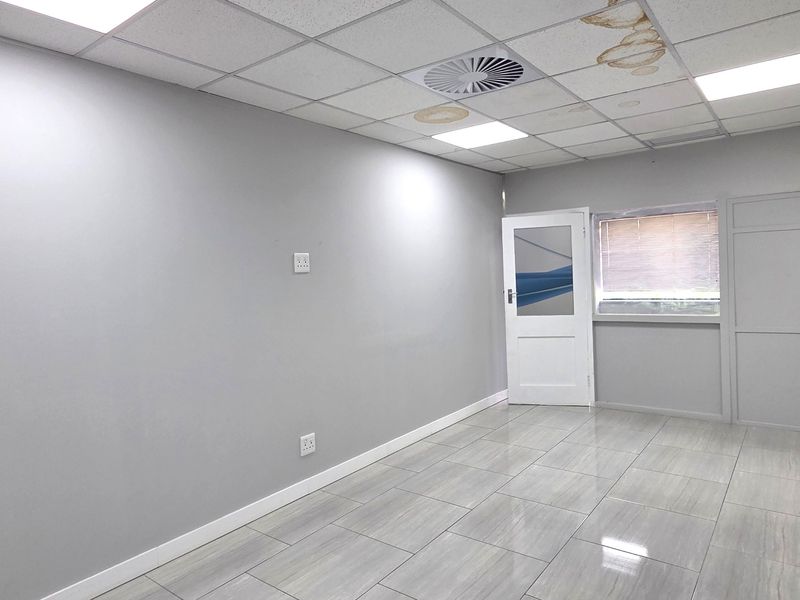 An empty office space featuring tiled flooring, a suspended ceiling with recessed lighting, and visible water damage on the ceiling tiles.