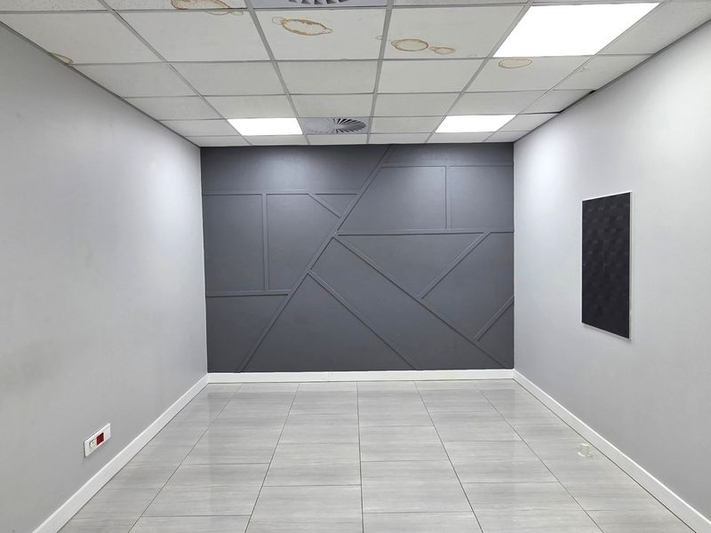 A vacant office space featuring a modern geometric feature wall, tiled flooring, and a suspended ceiling with recessed lighting.