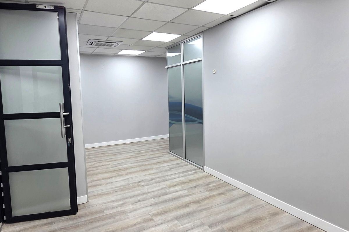 Modern, empty office space featuring neutral grey walls, wood-look laminate flooring, suspended ceiling with LED lighting, and contemporary glass partitioning.