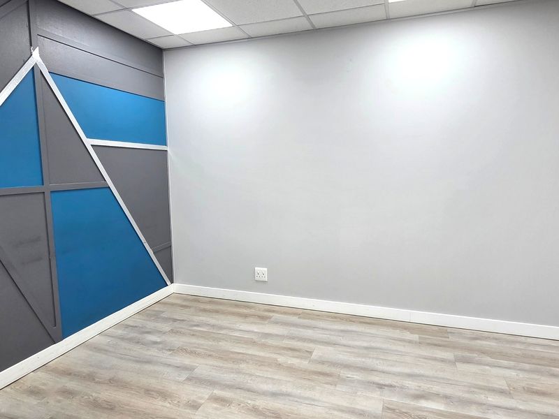 A clean, empty office space featuring modern laminate flooring, a suspended ceiling with recessed lighting, and a decorative accent wall.