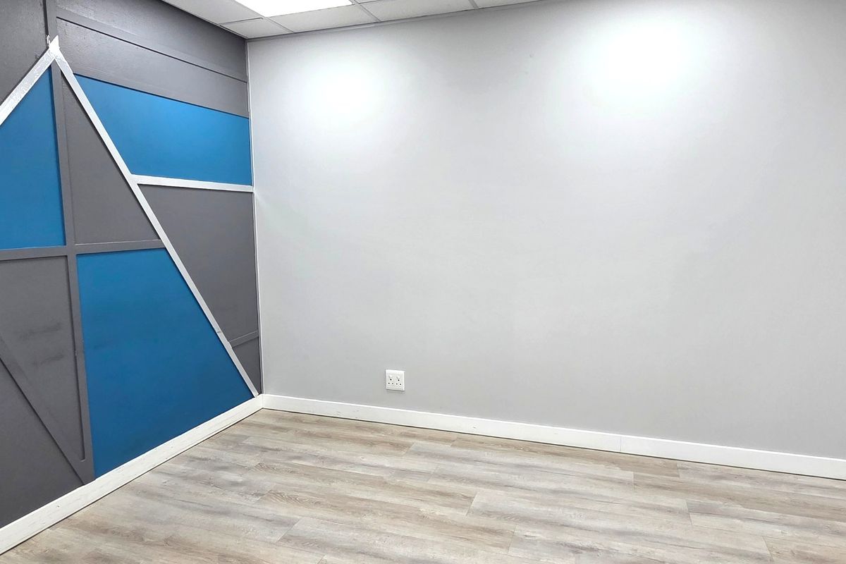 A clean, empty office space featuring modern laminate flooring, a suspended ceiling with recessed lighting, and a decorative accent wall.