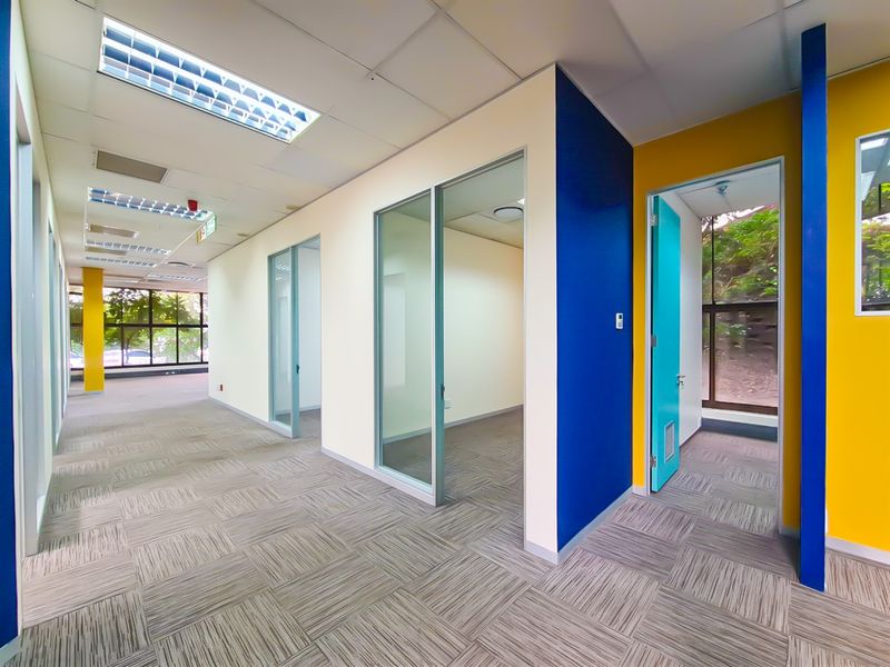 Modern office space featuring glass partitions, carpet tiles, and bright accent walls, offering a clean and professional environment for business operations.