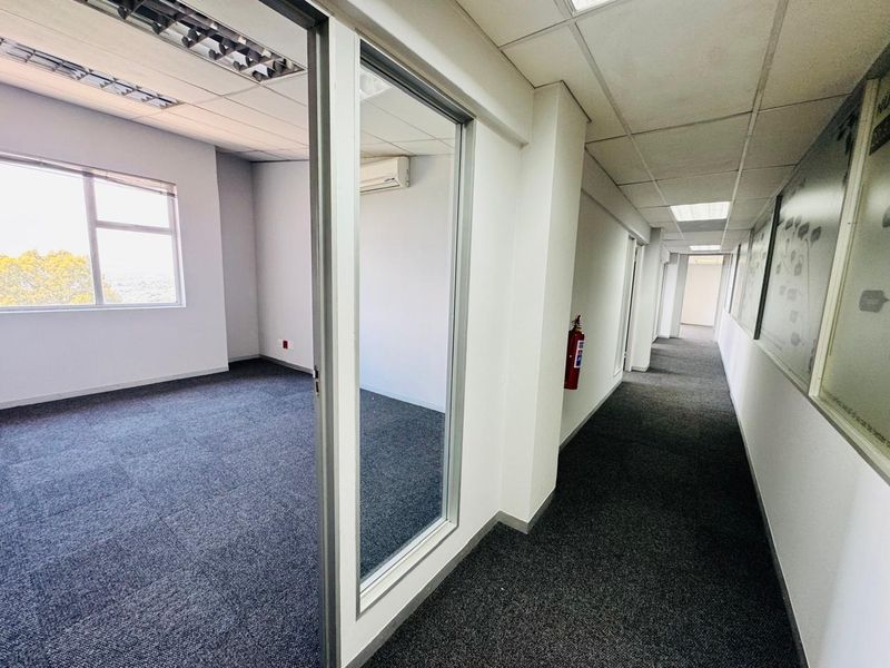 Empty office space featuring carpet tiles, suspended ceilings with recessed lighting, a glass partition wall, and a wall-mounted air conditioning unit.