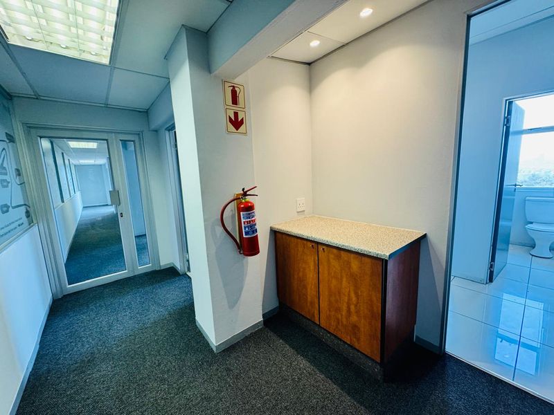 A functional office hallway featuring built-in cabinetry with a laminate countertop, recessed lighting, and a wall-mounted fire extinguisher.