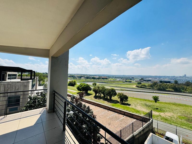 A spacious covered balcony featuring tiled flooring and metal railings, offering expansive elevated views over the surrounding landscape and race track.