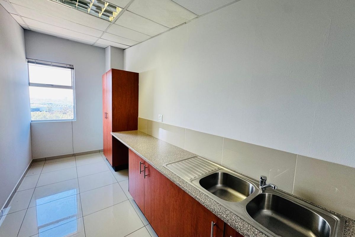 A clean, functional office kitchenette featuring built-in wooden cabinetry, a double stainless steel sink, tiled flooring, and ample counter space.